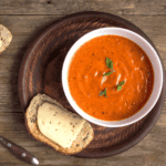 Tomato basil soup in a white bowl with bread and cheese