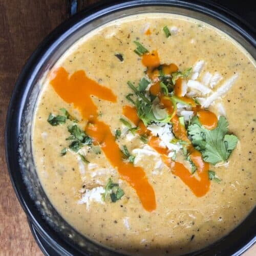 Bowl of queso with a hot sauce drizzle and cheese and cilantro garnish