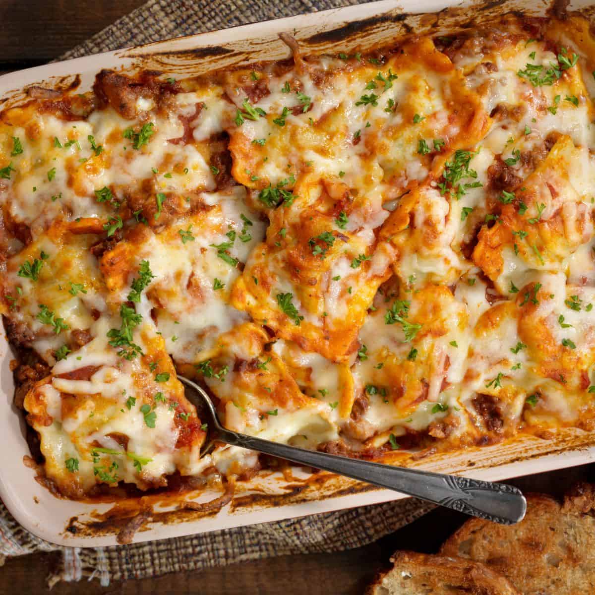 Finished ravioli lasagna in a white baking dish with a spoon