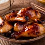 Chicken legs on a platter glazed with black garlic sauce. chopsticks in the background
