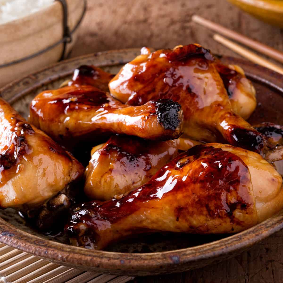 Chicken legs on a platter glazed with black garlic sauce. chopsticks in the background
