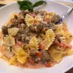 Italian Sausage Bow Tie Pasta in a white bowl with basil and a fork