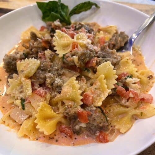 Italian Sausage Bow Tie Pasta in a white bowl with basil and a fork