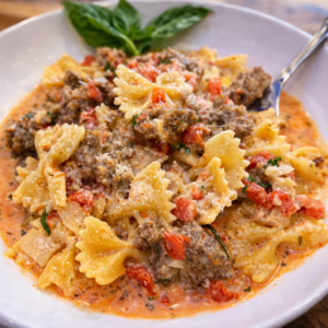 Italian Sausage Bow Tie Pasta in a white bowl with basil and a fork