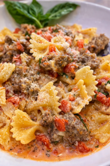 Italian Sausage Bow Tie Pasta in a white bowl with basil and a fork