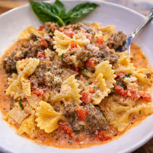 Italian Sausage Bow Tie Pasta in a white bowl with basil and a fork