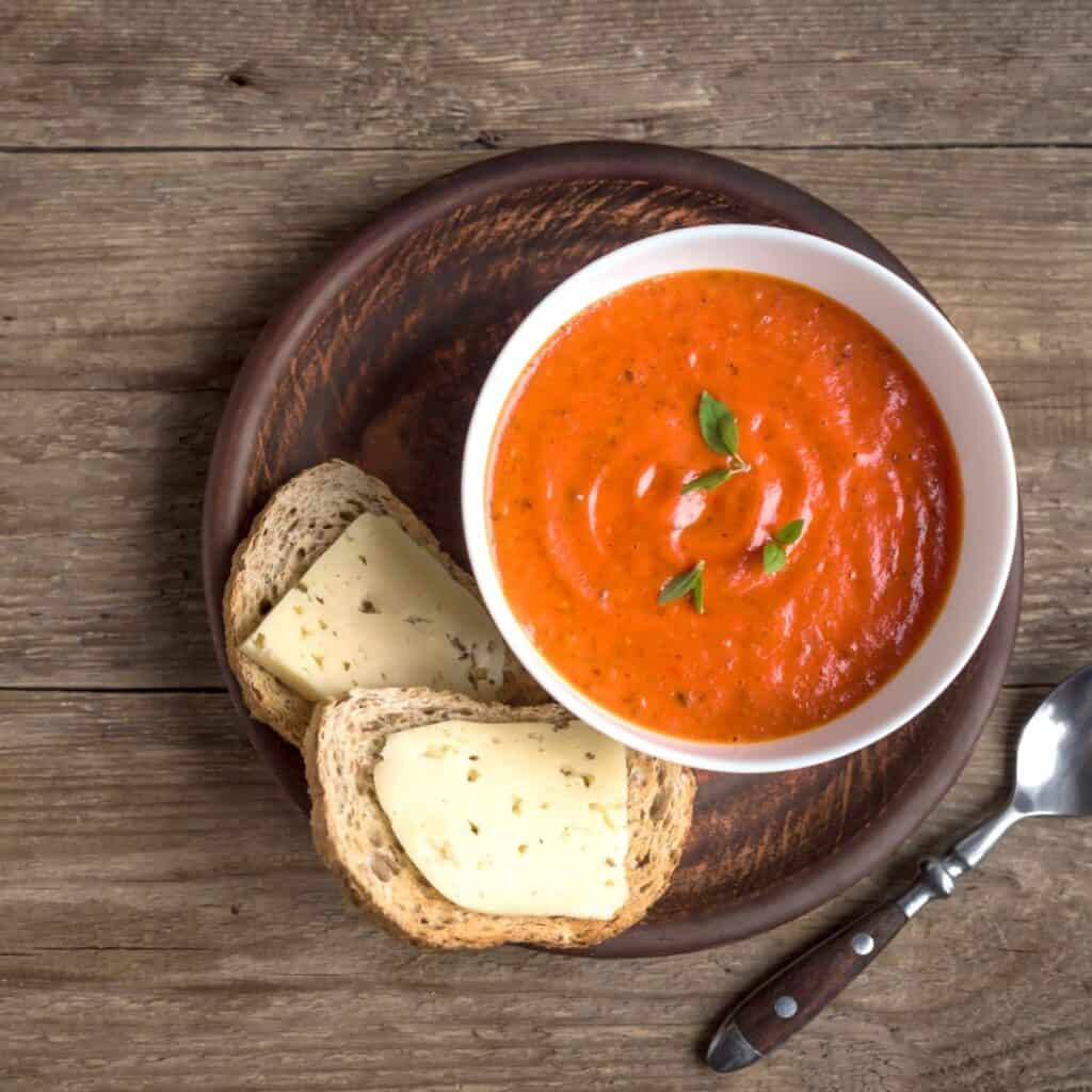 Bowl of tomato soup with bread and a spoon in the background