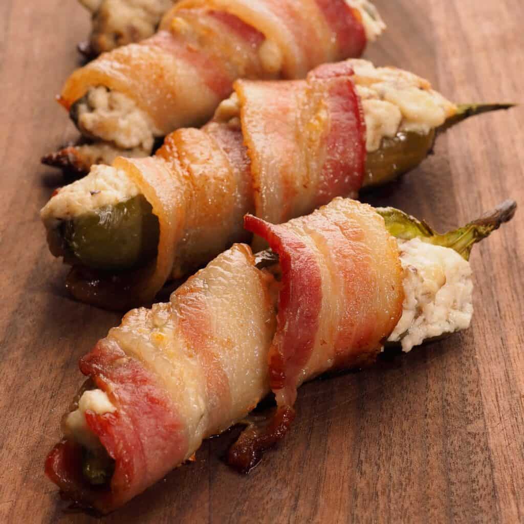 Bacon-wrapped jalapeño poppers stuffed with creamy cheese filling on a wooden board.