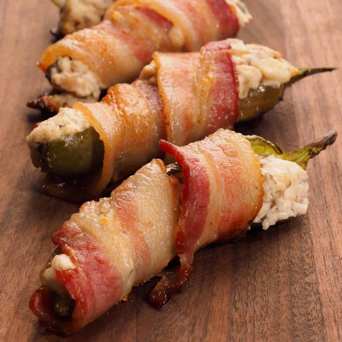 Bacon-wrapped jalapeño poppers stuffed with creamy cheese filling on a wooden board.