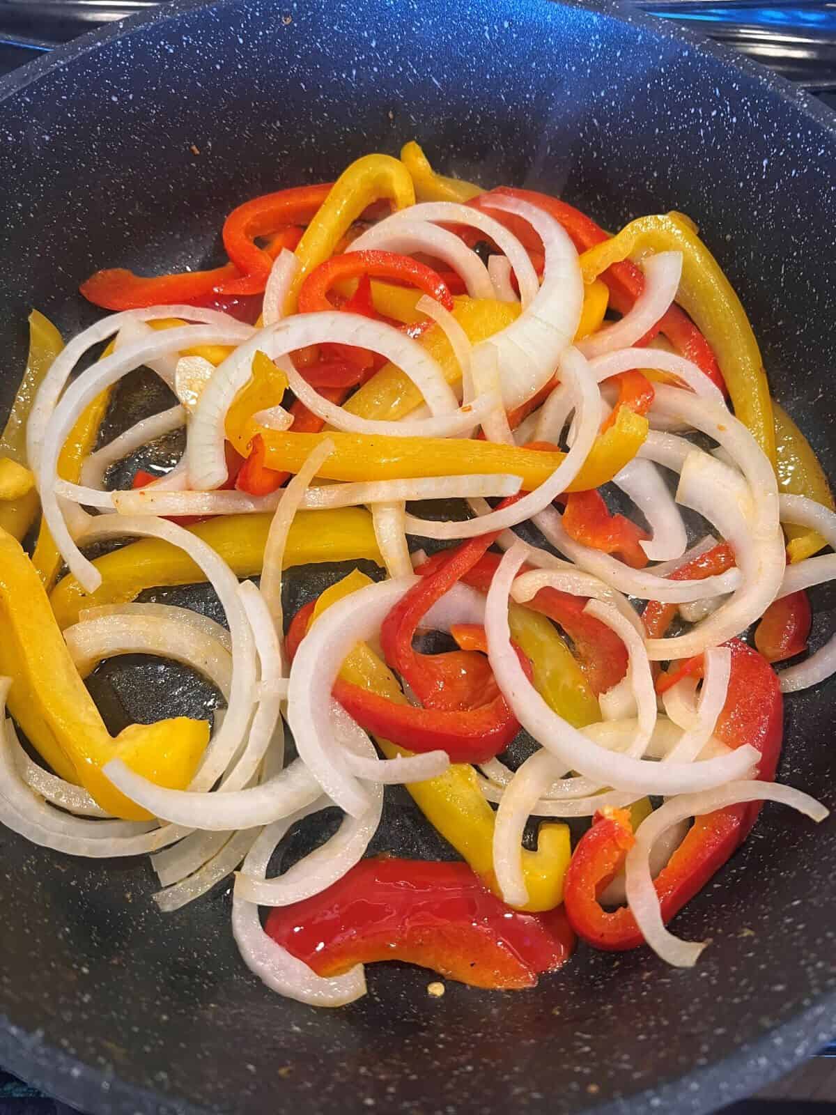 red and yellow pepper slices in a skillet with onions added