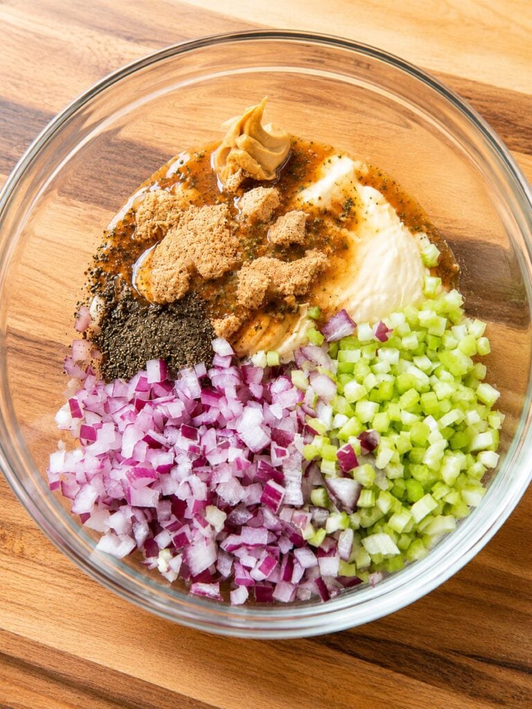 Diced purple onion, celery, mayo, ranch dressing mix, Dijon mustard, salt, and black pepper in a clear bowl