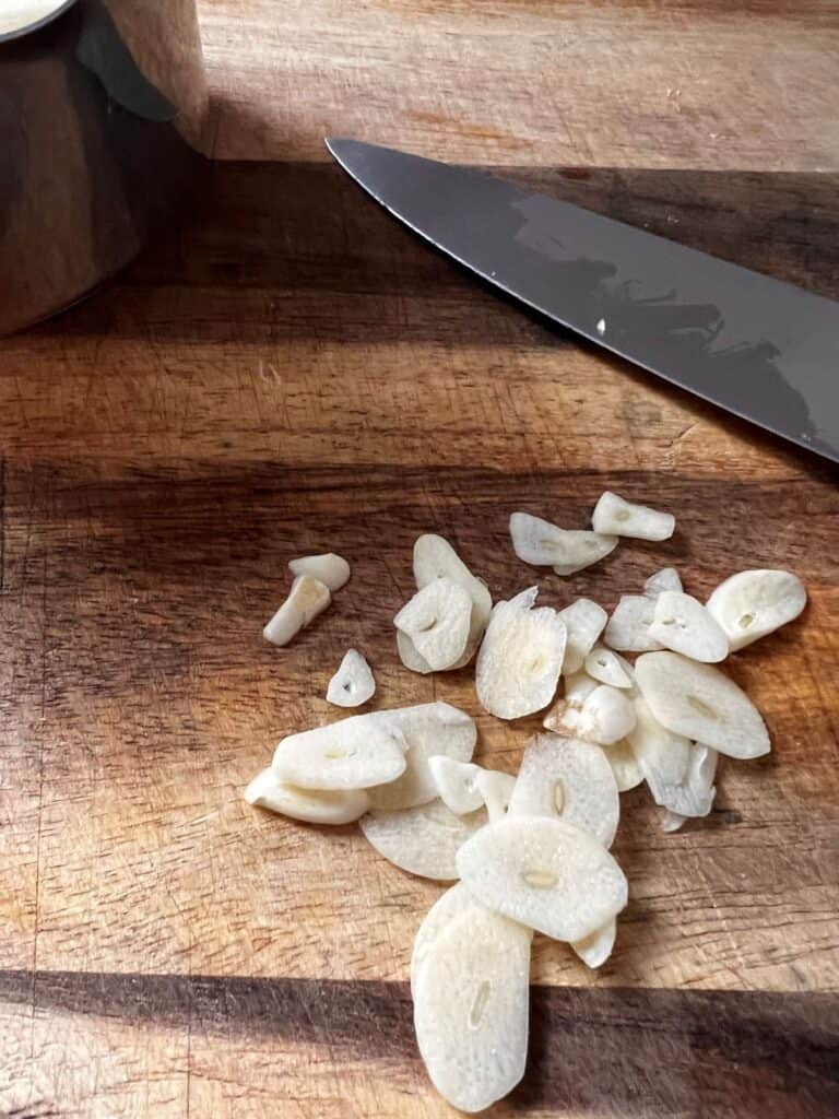 Thin cut garlic cloves and a knife on a cutting board