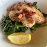 Finished dish. Tilapia filet on a bed of wilted spinach with crumbled bacon and a lemon wedge