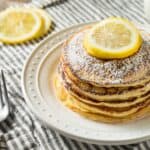 Finished pancakes on a white plate with powdered sugar and lemon slices