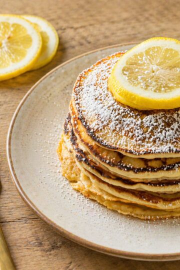 Finished pancakes on a beige plate with powdered sugar and lemon slices