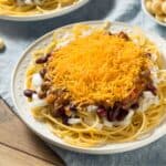 White plate with spaghetti smothered with chilli onions, and grated cheese. Cincinatti chilli