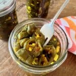 Jar of candied jalapenos with a fork in it.