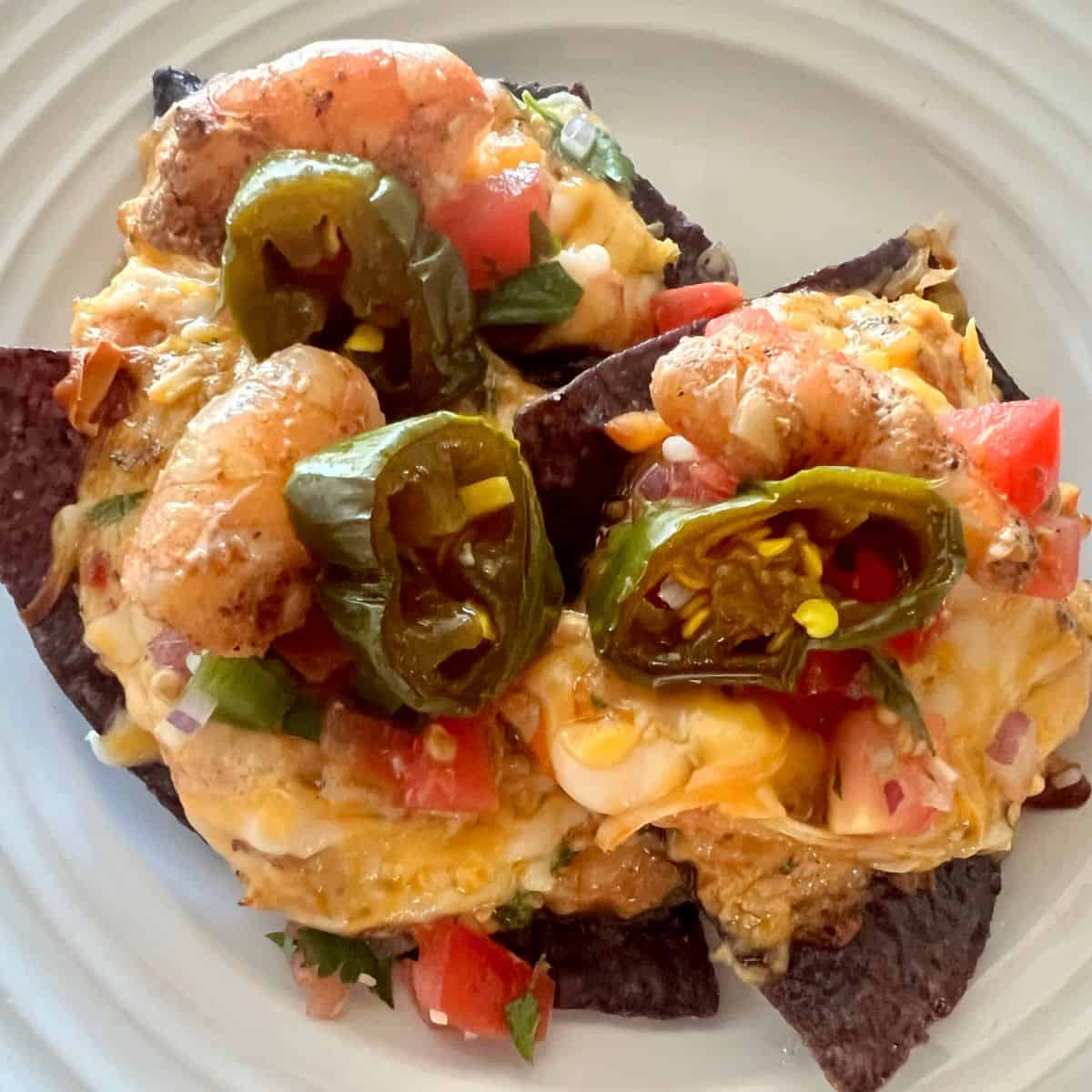 Three shrimp nachos on a white plate with pico and candied jalapenos