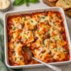 Finished ravioli lasagna in a white baking dish with a spoon