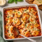 Finished ravioli lasagna in a white baking dish with a spoon