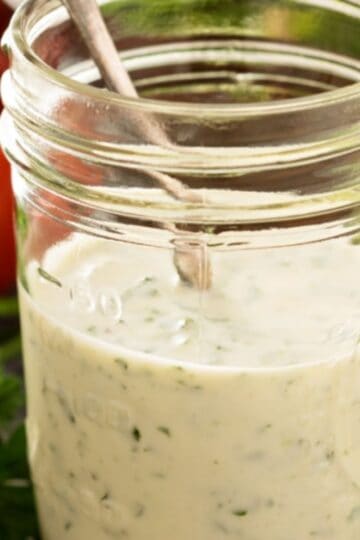 Caesar dressing in a mason jar with a spoon and vegetables in the background