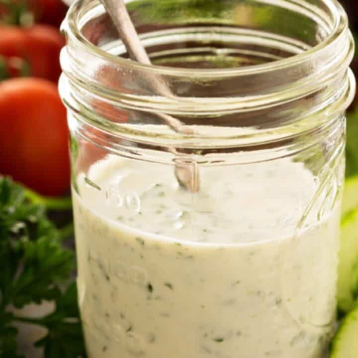 Caesar dressing in a mason jar with a spoon and vegetables in the background
