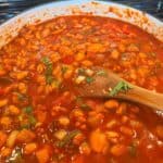 The finished Puerto Rican stewed beans (habichuelas guisadas) in their final form - a rich, reddish-brown stew with tender pinto beans, diced vegetables, and fresh cilantro visible throughout the thick, flavorful sauce.
