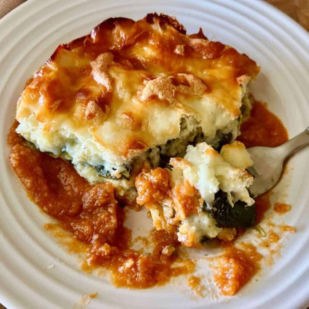 Finished chile relleno casserole on a white plate with red sauce and a fork