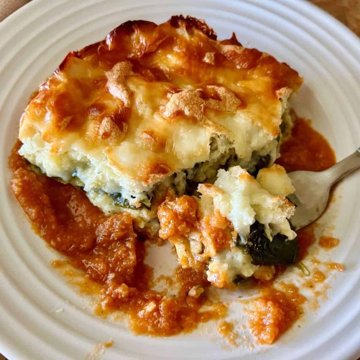 Finished chile relleno casserole on a white plate with red sauce and a fork