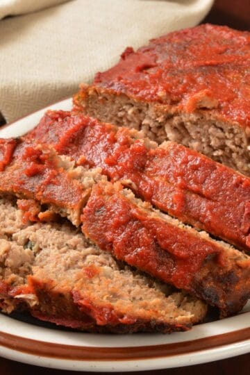Homemade meatloaf topped with tomato glaze, sliced and served on a white platter.