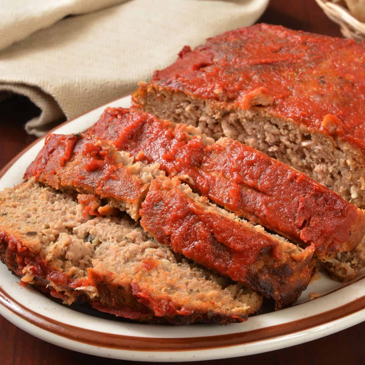 Homemade meatloaf topped with tomato glaze, sliced and served on a white platter.