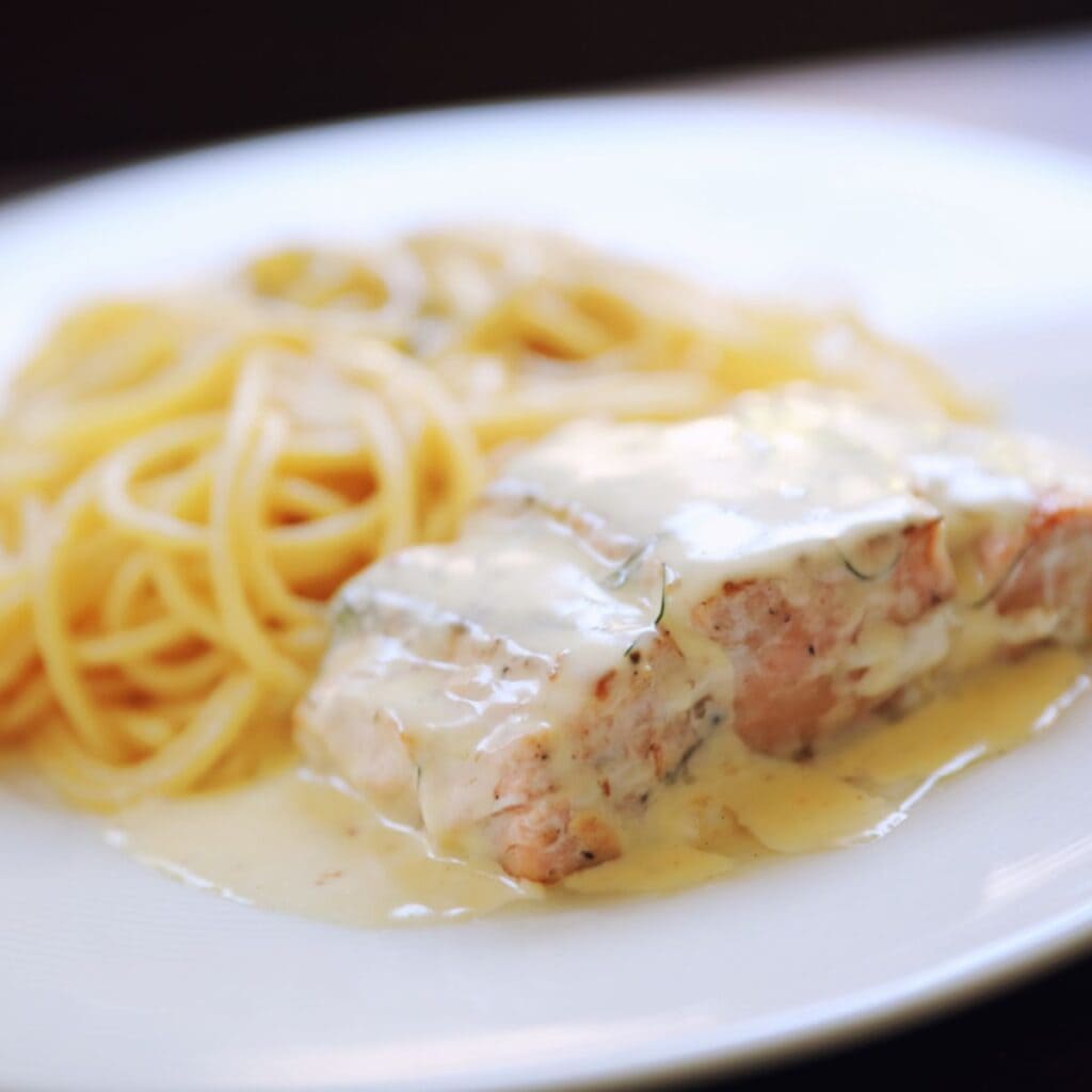 Salmon in creamy garlic sauce on a white plate with a side of pasta