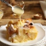 A slicee of bread pudding on a white plate with bourbon cream sauce being drizzled on top