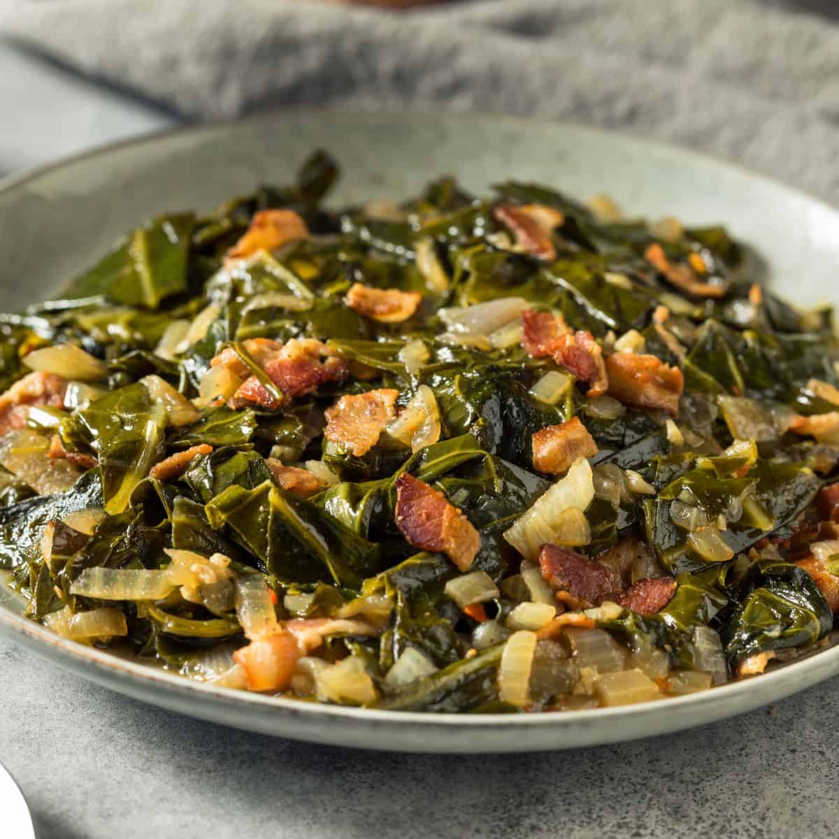 Large serving plate filled with Southern-style collard greens cooked with bacon pieces and diced onions, showing the dark green leafy vegetables glistening with cooking liquid on a gray speckled plate