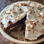 Slice of layered chocolate pie being removed, showing the distinct pecan crust, cream cheese, chocolate pudding, and whipped cream layers with pecan garnish on top.