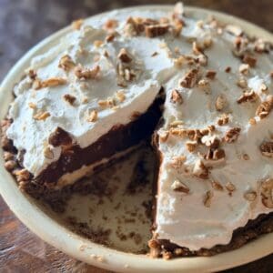 Slice of layered chocolate pie being removed, showing the distinct pecan crust, cream cheese, chocolate pudding, and whipped cream layers with pecan garnish on top.