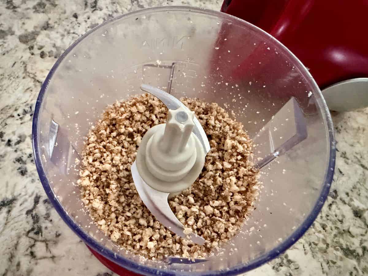 Finely ground pecans in a food processor bowl after processing, creating a crumbly, sandy texture.