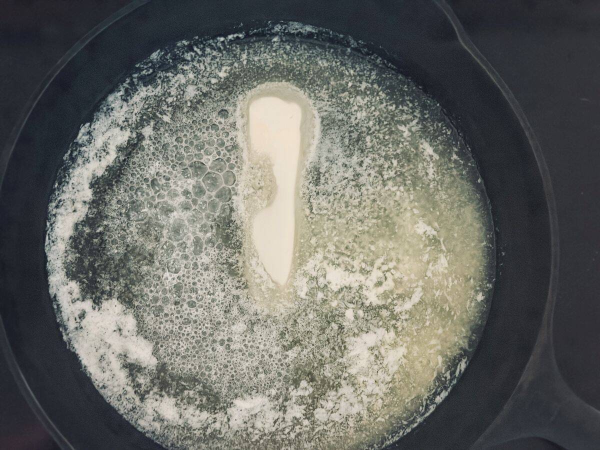 Butter melting in a black pan or skillet with visible bubbling and foam.