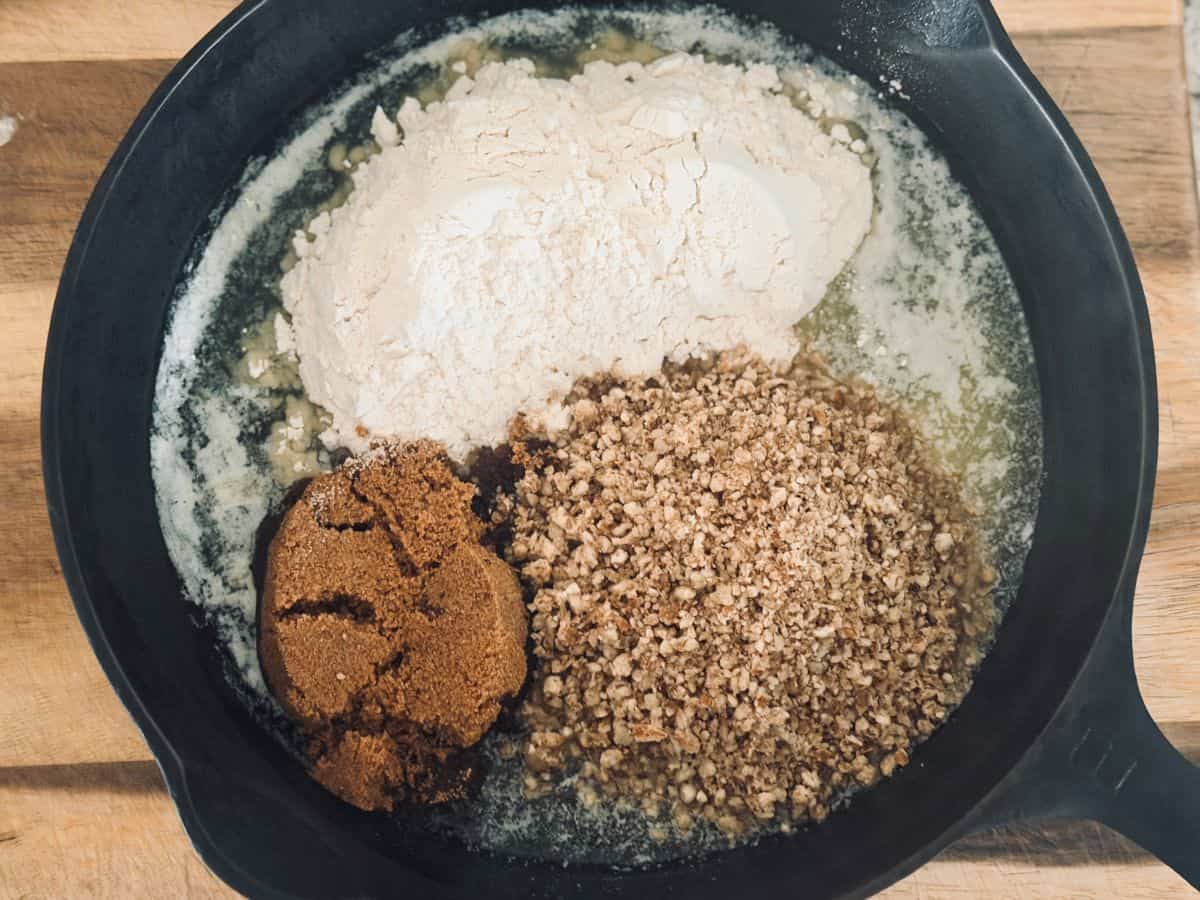 Ground pecans, brown sugar, and flour added to melted butter in a black skillet, shown before mixing.