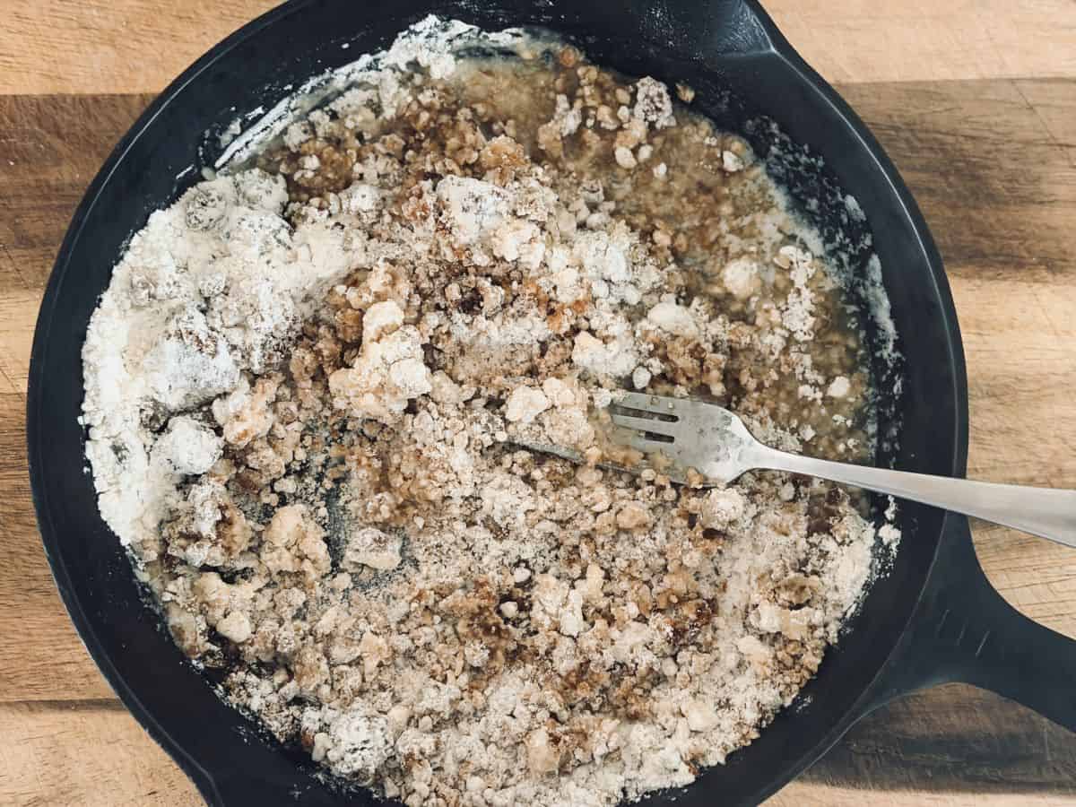 Pecan crust mixture being combined with a fork in the black skillet, showing a crumbly, sandy texture throughout.