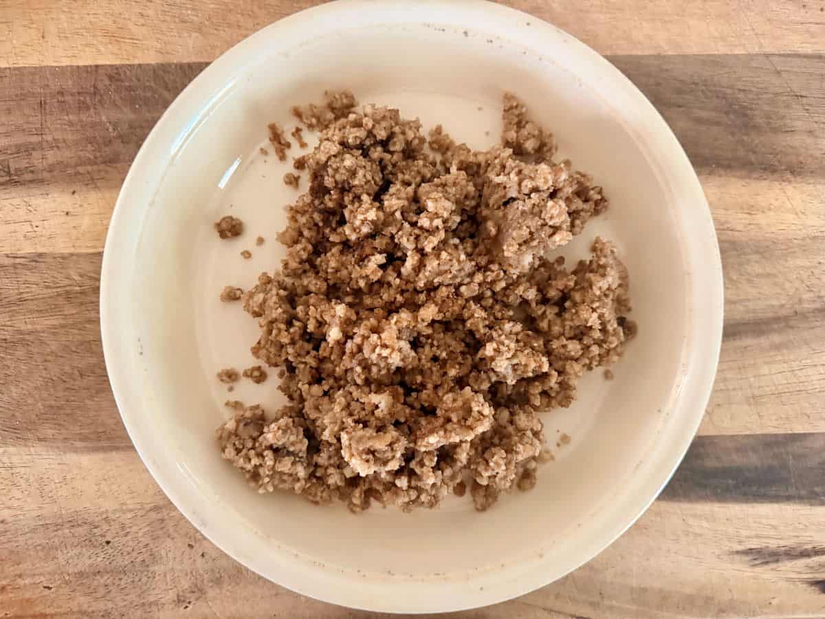 Finished pecan crust mixture removed from the skillet and placed in a white bowl, showing an even, crumbly consistency.
