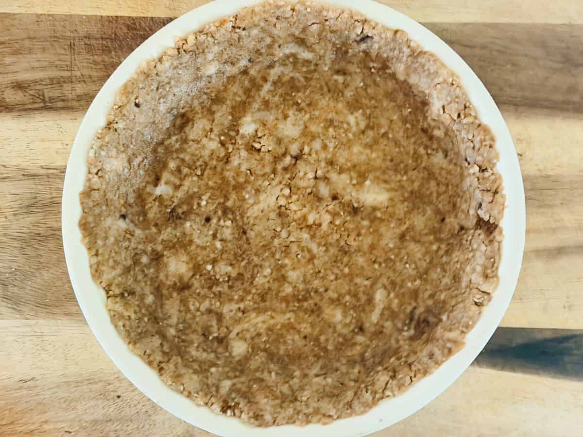 Pecan crust pressed into the bottom and up the sides of a white pie plate, forming an unbaked pie shell.