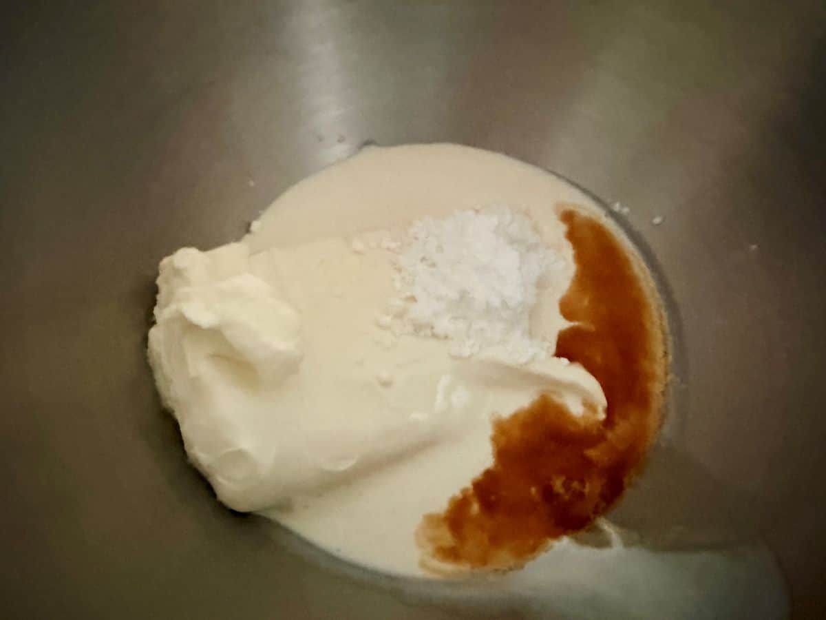 Cream cheese, powdered sugar, and vanilla extract in a metal mixing bowl, shown before beating together.