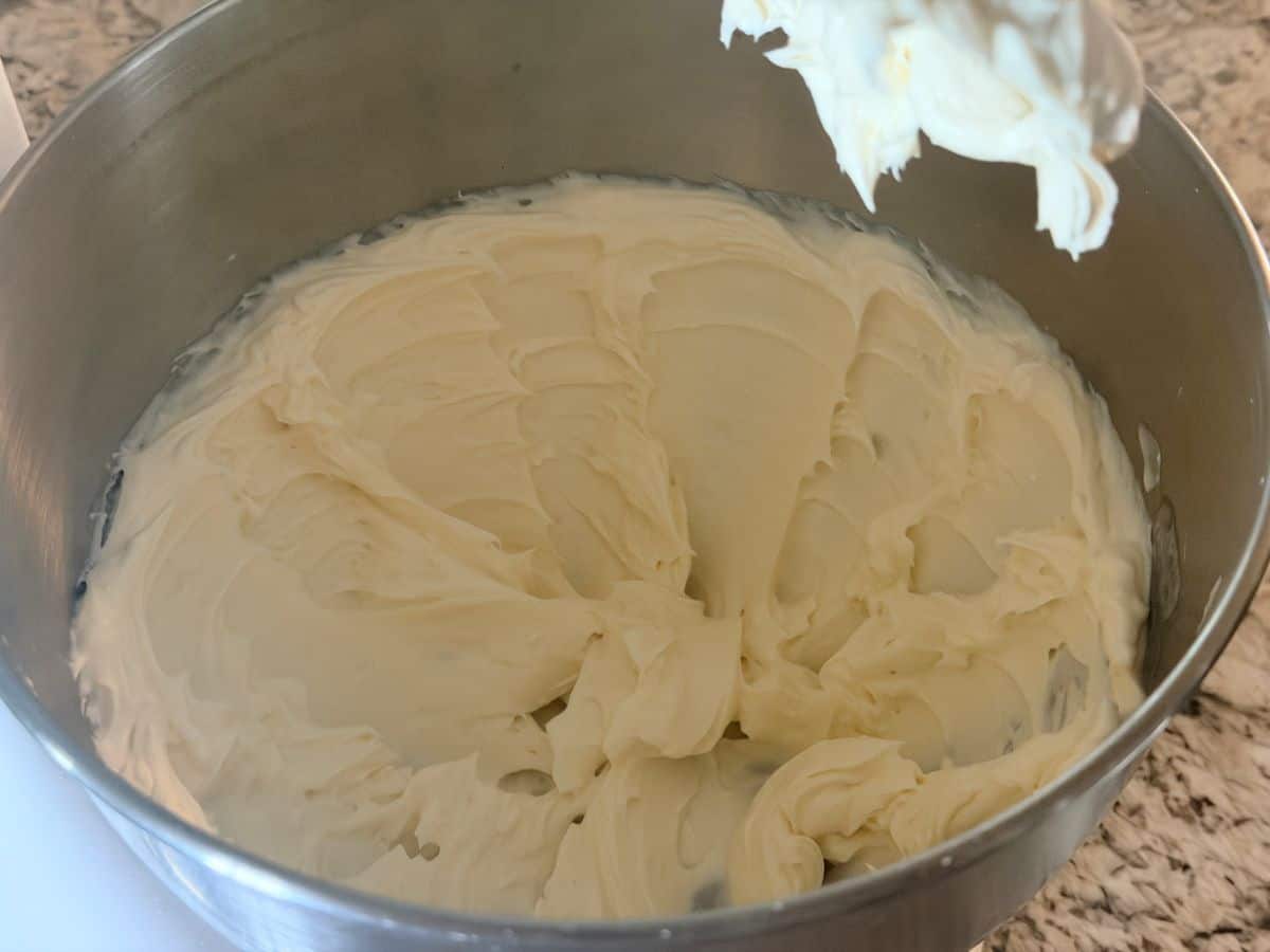 Whipped cream cheese mixture in a metal mixing bowl, showing a smooth, fluffy white consistency.