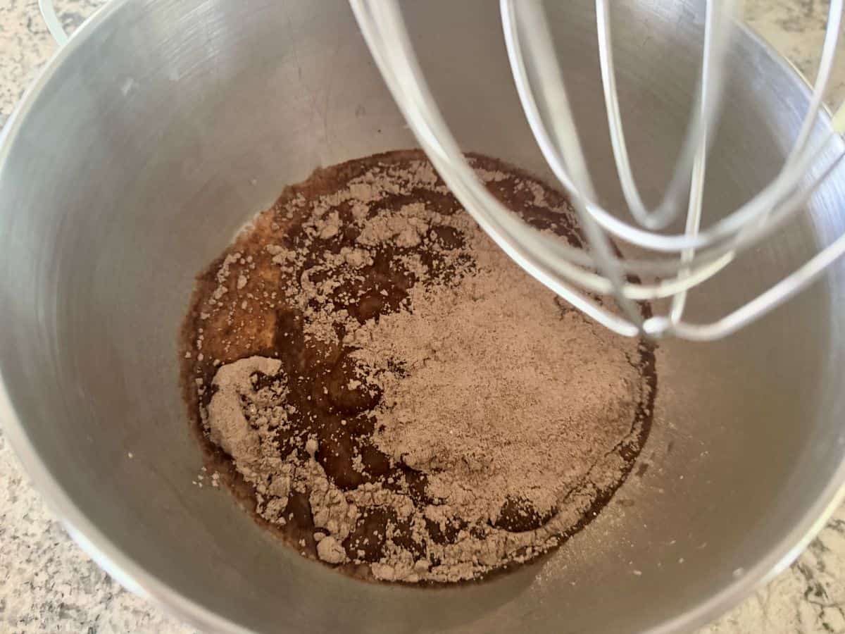Chocolate pudding mixture being prepared with a hand mixer in a metal bowl, showing dark brown pudding with beater attachments visible.