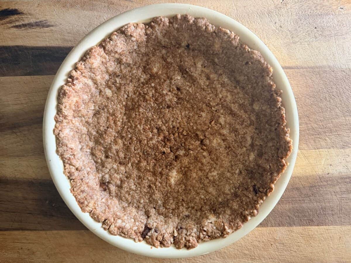 Baked pecan crust in a white pie plate, showing a darker, set appearance after baking.