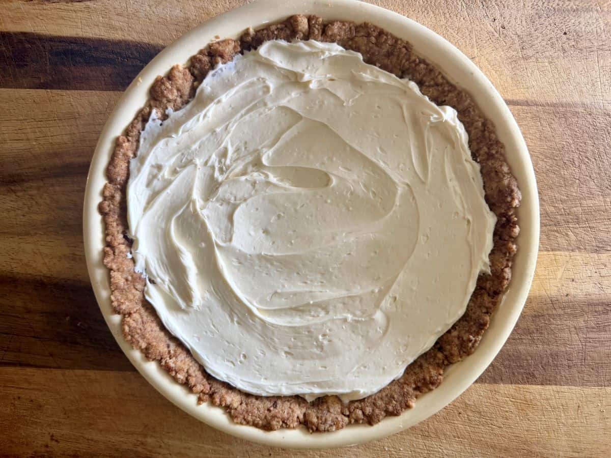 White cream cheese layer spread over the baked pecan crust in the pie plate.