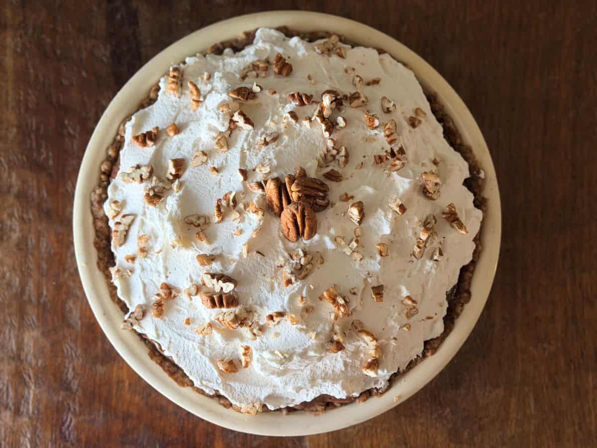 Finished pie topped with whipped cream and garnished with chopped pecans, shown from above.