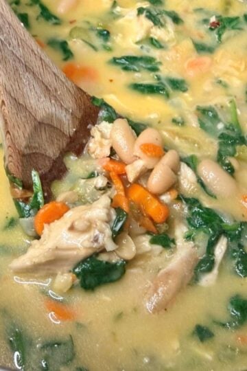 Close-up of creamy chicken and white bean soup with spinach, carrots, white beans, and chopped chicken.