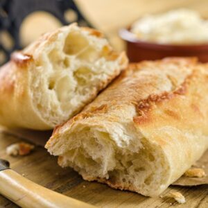 finished mini baguette torn in half on a cutting board with a bowl of butter in the background.